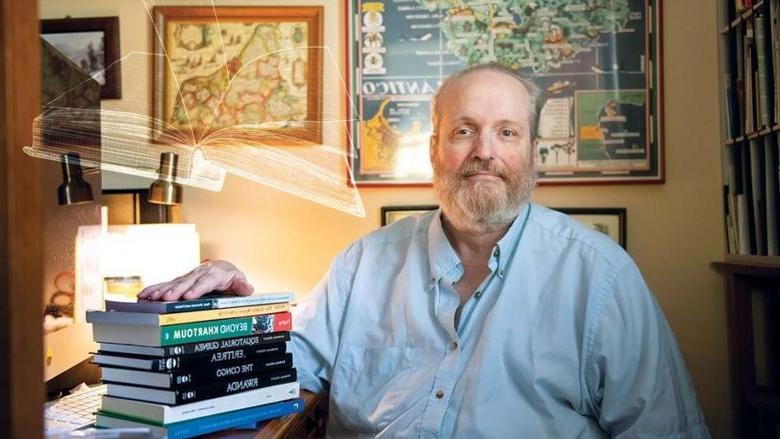 Randall Fegley sits at desk with books on top of it